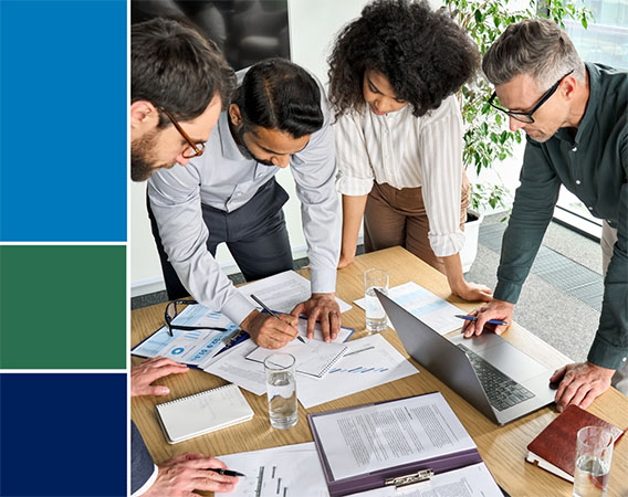 Group of four adults leaning over a table that has papers on it