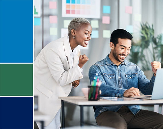 Two business people, one woman, one man, looking over at laptop, smiling, fist pump