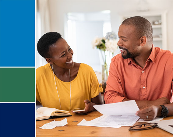Older black couple sitting at a table, smiling at each other, reviewing paperwork